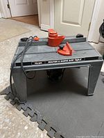 Image of Hirsh router and sabre saw table from side angle showing table top, legs, cord, and red attachments