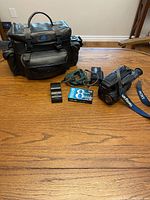 Sony Handycam camcorder with strap, charger, battery, unopened 8mm tape, and camera bag on wooden table.