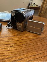 Front side of Sony Handycam digital camcorder showing lens with cover and flip-out LCD screen labeled Handycam.