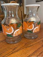 Two curved glass jars decorated with orange slices and green leaves on a wood table.