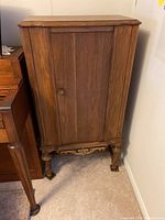 Front angle view of the solid wood cabinet showing door, legs, and carved bottom edge.