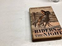 Photo showing the front cover of the 1932 book 'Riders of the Night' by Eugene Cunningham with cowboy horse rider illustration on dust jacket.