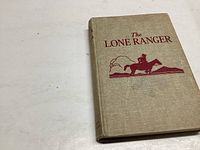 Front cover of the 1936 Lone Ranger book with beige cloth and red print illustration.