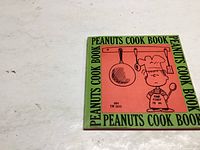 Front cover of the cookbook showing Charlie Brown in chef's attire with kitchen utensils around him, titled 'Peanuts Cook Book'.