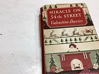 Close-up photo of the front cover of the book titled Miracle On 34th Street by Valentine Davies showing vintage holiday illustrations.