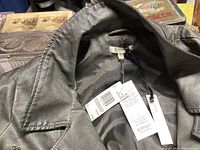 Close-up of Buffalo leather jacket collar, interior lining, and attached tags showing new condition and size XL.