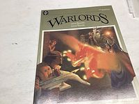 Photo of the 'Warlords' graphic novel cover showing title, creators' names, and cover art featuring fantasy characters and a dragon-like figure.