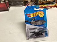 Unopened Hot Wheels 2013 Star Trek USS Vengeance collectible toy in blister packaging on a white table with miscellaneous items in background