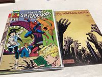 Six comic books with visible titles including Amazing Spider-Man #2 and The Walking Dead #116 on top of a table.