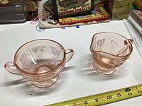 Pink depression glass sugar bowl and creamer side by side on table with ruler showing size