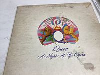 Front cover of Queen 'A Night At The Opera' vinyl album showing colorful emblem of winged crest with two lions and album title text.