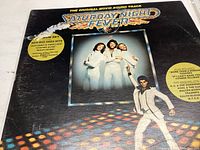 Front cover of Saturday Night Fever soundtrack album with three Bee Gees and dancer in white suit, showing faint scratches.