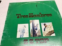 Front cover of ZZ Top Tres Hombres vinyl album with green background, title, band photos and wear visible.