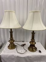 Two brass table lamps on a table, showing overall condition and cream white shades