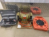 Bench grinder, Dremel tool with accessories case, and orange extension cord on floor in front of diamond plate metal wall