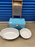 Full view of the blue Coleman cooler with two white enamel pots in front and wooden washboard behind