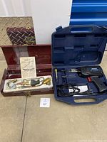 Both the soldering machine in a blue case and the torch set in a red metal box are shown on the floor.