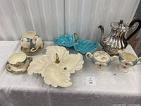 Tea pot with acorn decor lid, cream and sugar set, four cups and saucers, blue and white leaf shaped sectioned serving dishes on table.