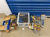 Wide view of a milk crate and boxes filled with assorted nails, screws, staples, and hardware including door hinges and stops.