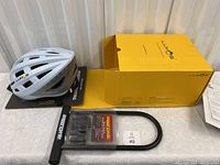 Photo showing white Lumos Kickstart bike helmet, yellow Lumos box, and Supercycle steel U-lock in packaging.