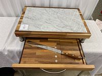 Top view of marble cutting board on wooden base with pull-out drawer open exposing interior and knife.