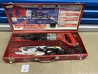 Milwaukee Sawzall Plus heavy duty reciprocal saw in an open red metal case with assorted blades laid in the case.