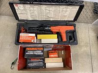 Remington RAM powder-actuated fastening gun in black case with multiple boxes of powder-actuated fasteners.