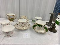 Six tea cups and saucers with two vintage metal candle holders arranged on white cloth