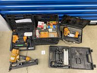 Overview photo showing three Stanley Bostitch pneumatic nailers in black cases and a black crate with multiple boxes of nails and staples