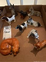 Nine ceramic dog and fox figurines in a cardboard box, different poses and colors