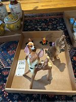 Tray with a ceramic Bambi figurine in foreground, dog figurine, and small character figurines including Winnie the Pooh and others in background on a patterned rug.
