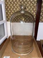 Full view of clear glass bell jar with knob handle on top, round dome shape visible against woven background.
