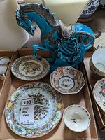 Photo showing the blue glazed ceramic horse statuette positioned above several porcelain plates and bowls laid in a cardboard box.