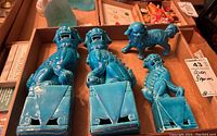 Photo showing three turquoise ceramic foo dog figurines on triangular bases and one smaller foo dog figurine inside a box.