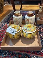 Photo showing 2 matching yellow lidded containers and 2 matching cream-colored jars with floral and bamboo designs in a box on carpet.