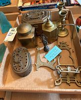 Photo showing the collection of various vintage and antique brass items including candlesticks, lidded boxes, brass stands of different designs, and a small figurine.