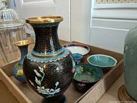 Photo showing multiple cloisonne vases with gold rims and several porcelain bowls in cardboard trays.