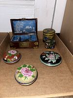 Photo of the open oriental wooden jewelry box showing blue fabric interior compartments alongside three ornamental cloisonné jars with floral motifs.