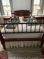 Full view of the wooden full bed frame showing the headboard, footboard with spindle detailing, and white bedding with various jars and items on top of mattress area.