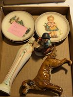 Overview photo showing all figurines and collector plates inside a cardboard box, with sticky note indicating 'All Goebel.'