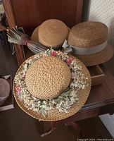 Three woven straw hats and one vintage umbrella arranged on a wooden surface near a cabinet.