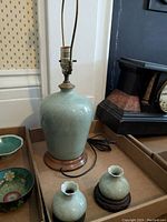 Porcelain lamp base on wood stand with two matching small vases on wood stands beside it, lamp cord visible, no shade included.