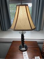 Side view of one lamp showing twisted black and gold column with round base and beige fabric lampshade with brown trim