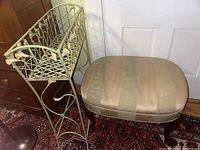Metal planter stand next to upholstered ottoman on patterned rug.