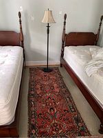 Photo showing vintage carpet runner between two wooden beds with floor lamp at the end