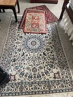 Four rugs arranged, including one large cream and blue Persian-style rug, and three smaller rugs stacked and scattered