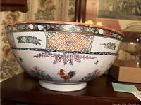Side view of large porcelain bowl with rooster and floral hand-painted designs and decorative border on rim.