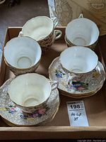 Top-down view of five floral Spode teacups paired with matching saucers, showing gold trim and multicolored flowers.