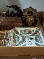 Wide view of the lot showing all items in a box on surface, includes carved wooden boxes, serving dishes, condiment dishes, brass-accented box, and wood carving
