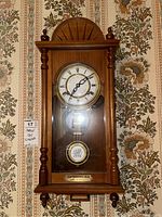 Full view of the wooden framed wall clock with decorative accents and glass front.